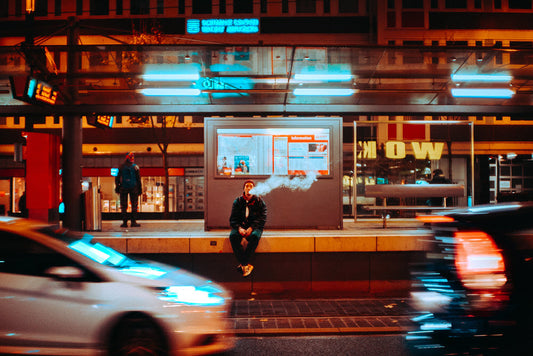 Vaping man sitting on city ledge watching traffic. Photo by Mika Baumeister on Unsplash