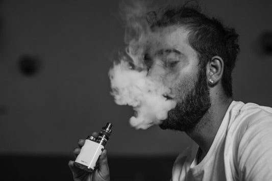 Man with beard vaping from vape device, smoke covers face. Photo by Sven Kucinic on Unsplash