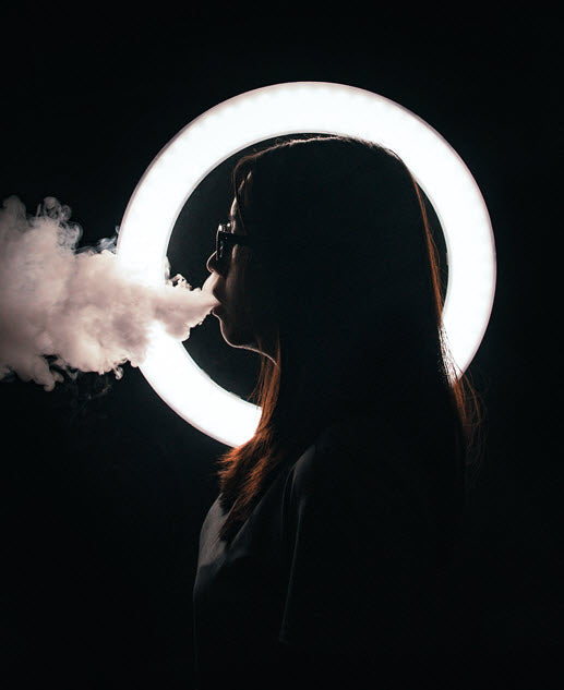 Side view of woman smoking with illumination in the background. Photo by John Caroro on Unsplash